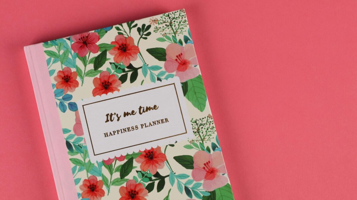 Floral-patterned happiness planner with the text 'IT'S MY TIME' on the cover, placed on a pink background