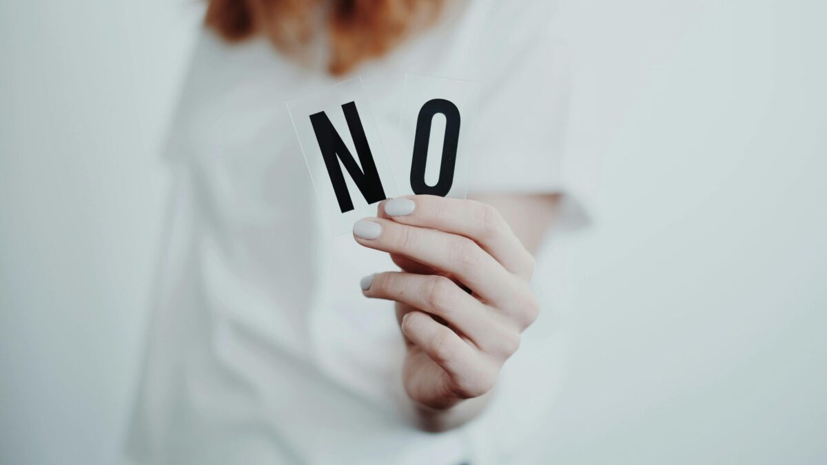 Person holding the letters 'N' and 'O' to form the word 'NO', with a neutral background