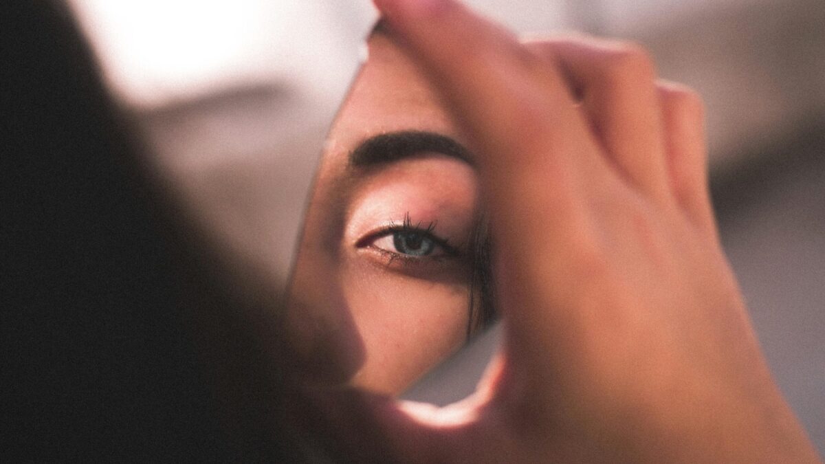 Close-up of a person holding a small mirror in front of their eye, reflecting the eye and part of the face
