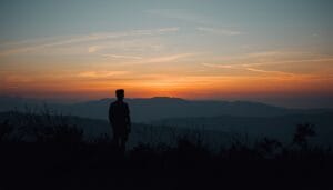Person standing quietly at sunrise overlooking mountains symbolizing reflection, grounding rituals, and reconnecting with oneself